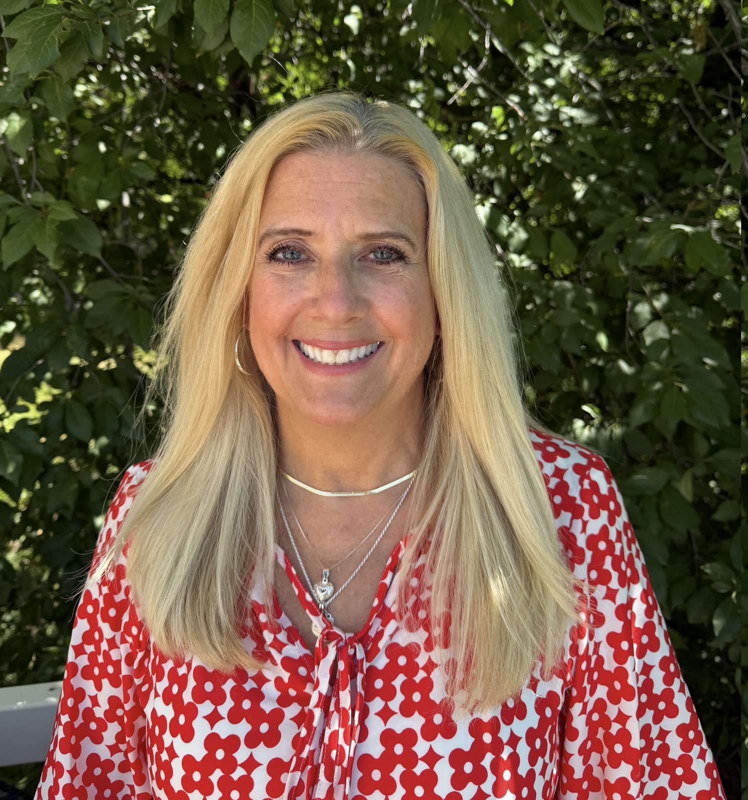 Denita Mortensen, CMHC, NCC, smiling outdoors in front of greenery